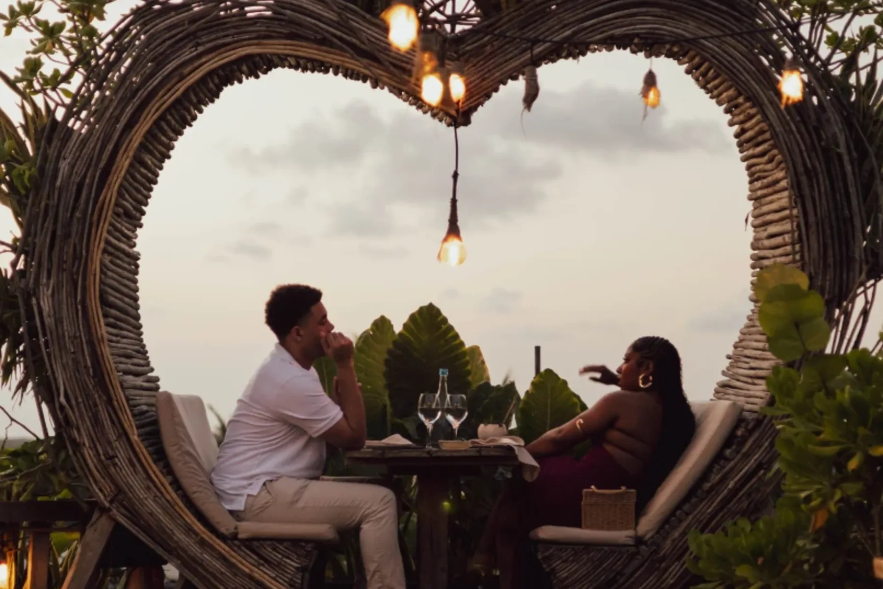 Couple dining in a heart-shaped wicker frame at sunset.
